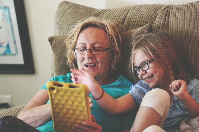 Older adult female and young girl play with a tablet while sitting in a recliner