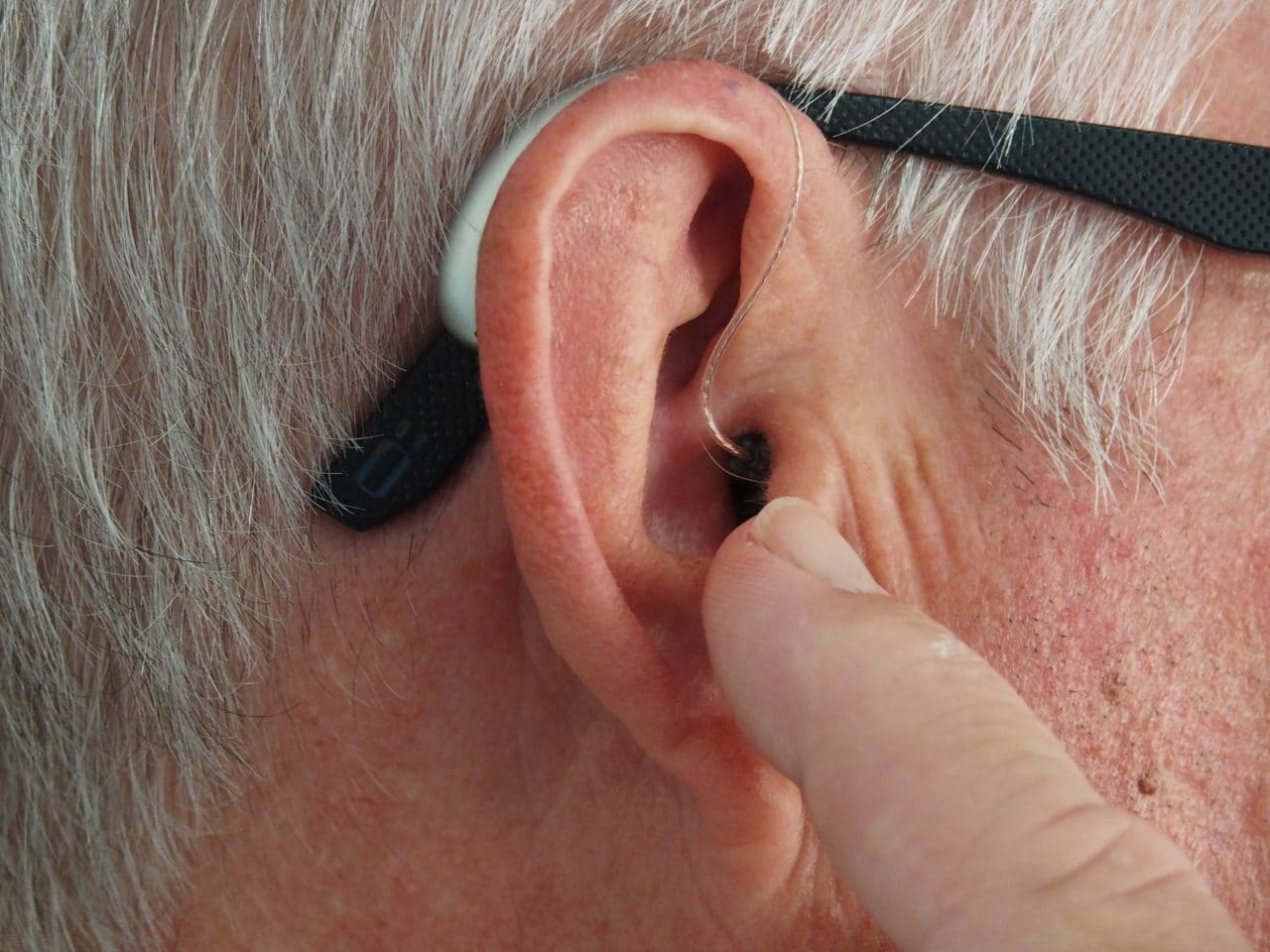 Man points at hearing aid on ear