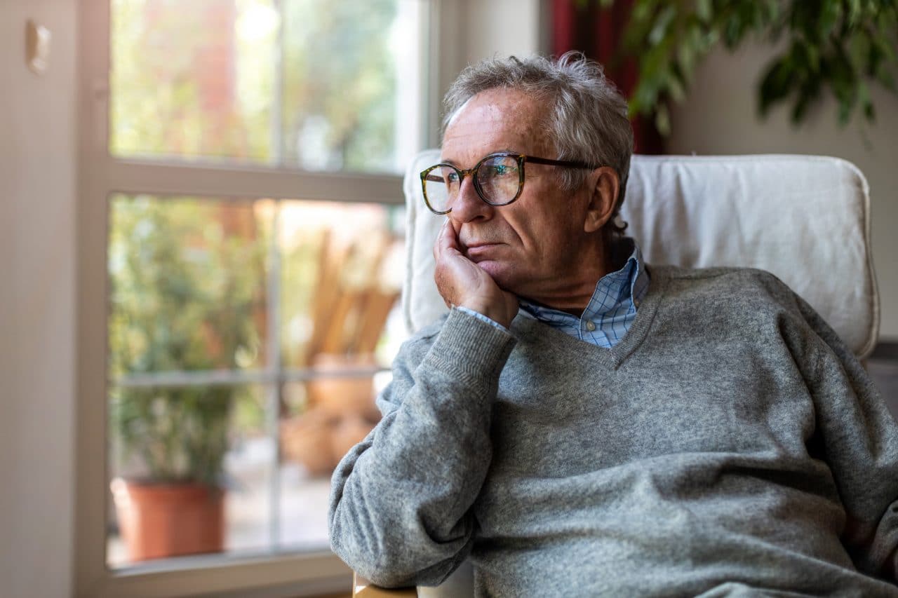 Older man looking out of window at home.