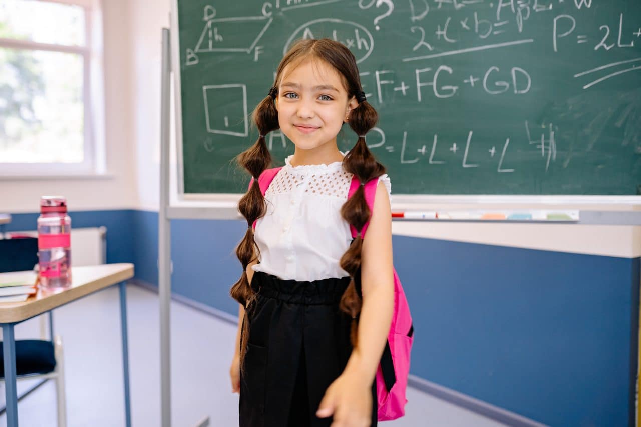 Young girl standing in front of a chalkboard on the first day of school.
