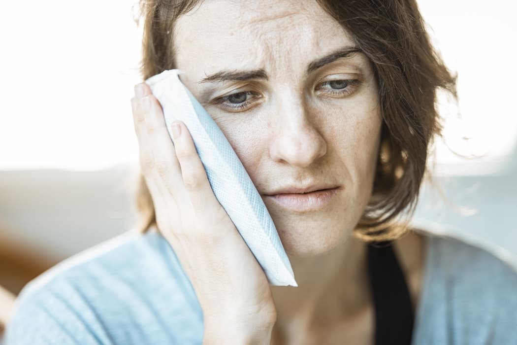 Woman holding a cold pack  up to her face.