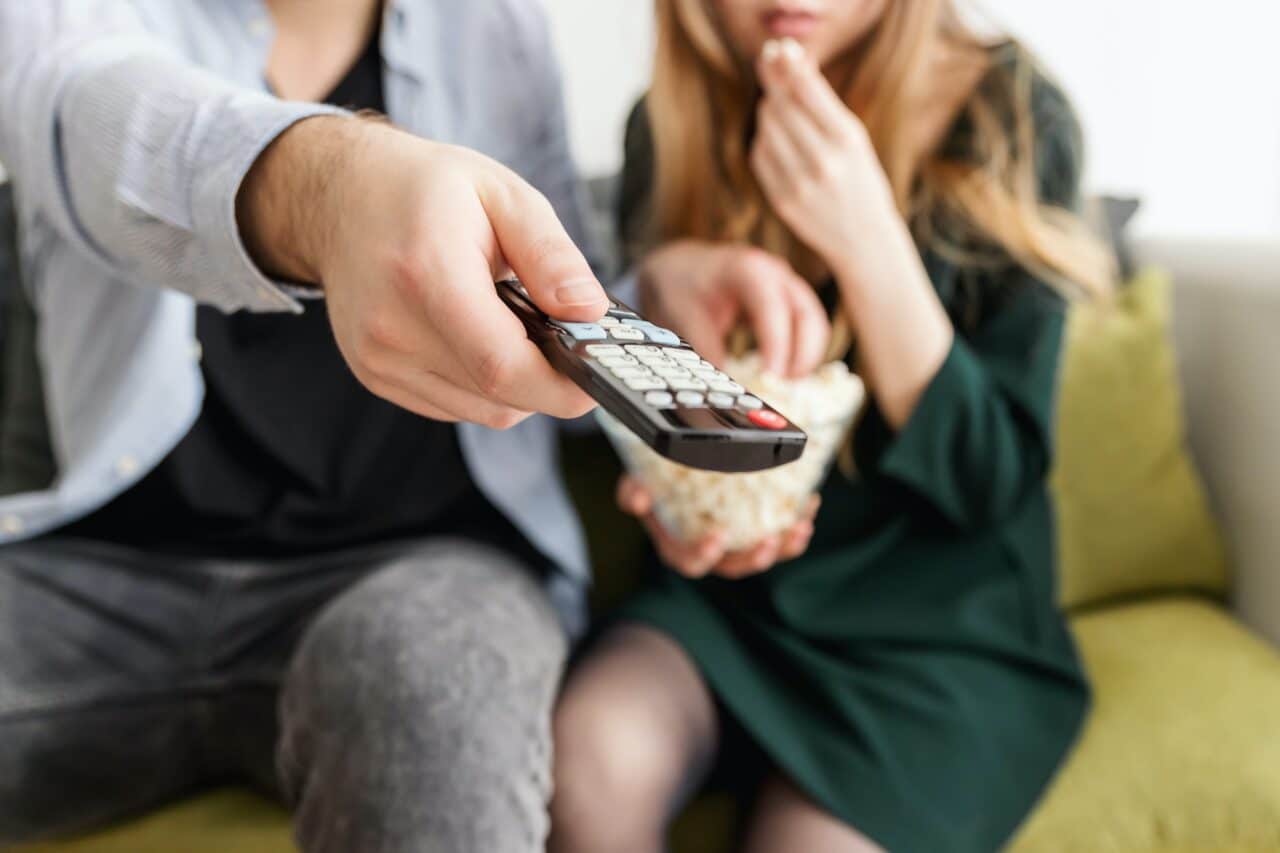 Close up of a couple watching TV with the man holding the remote.