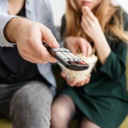Close up of a couple watching TV with the man holding the remote.