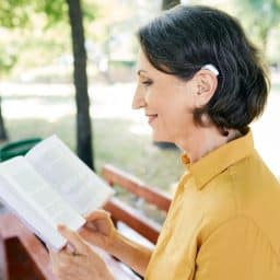 Senior woman with hearing aids smiling and reading in the park.