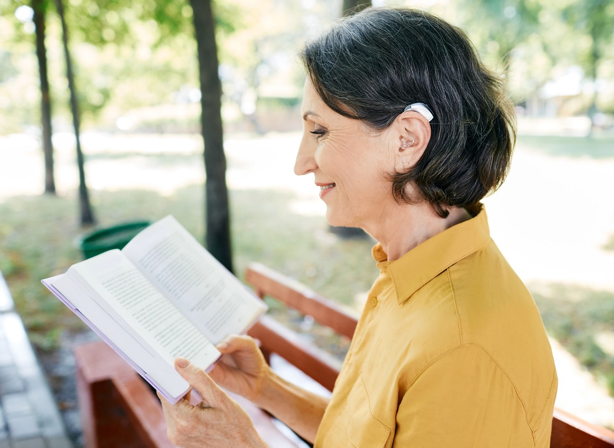 Senior woman with hearing aids smiling and reading in the park.