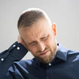Man experiencing tinnitus holding his ears looking upset