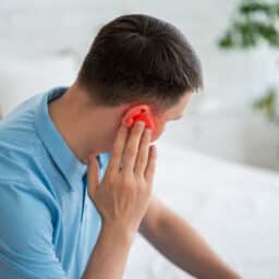 Man with tinnitus holding his red ear