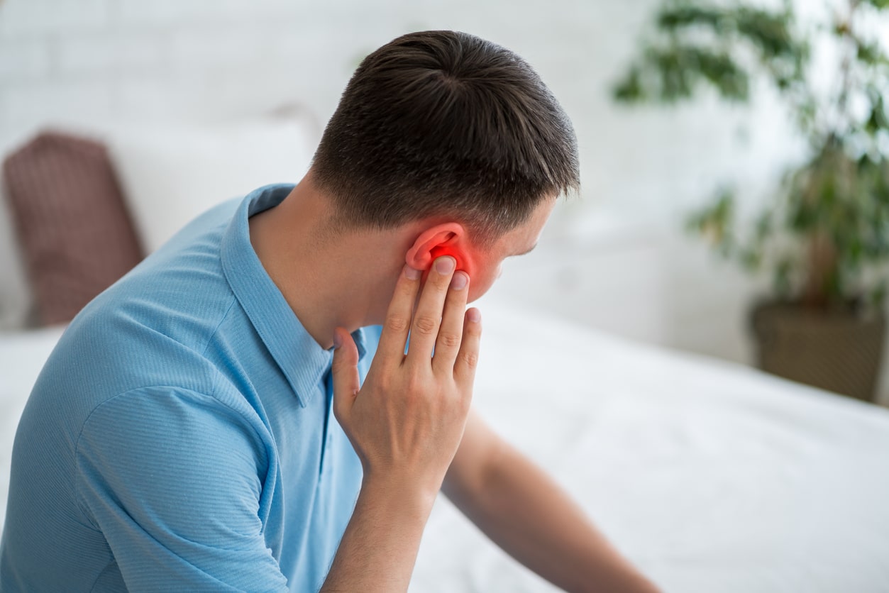 Man with tinnitus holding his red ear.