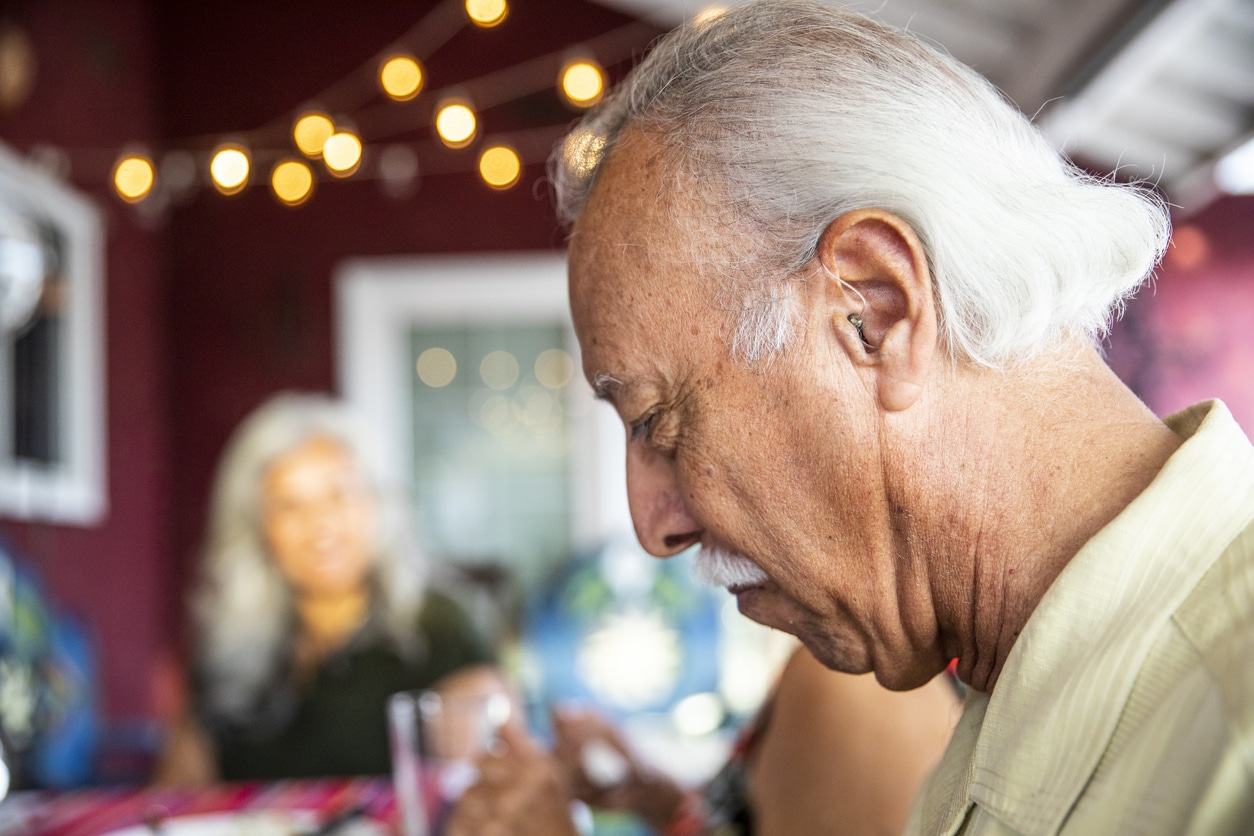 Man with a hearing aid eating with many people in a restaurant. 