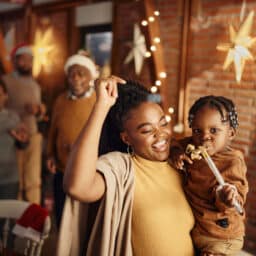A family celebrates the holidays at a holiday party. A dancing woman holds a child.