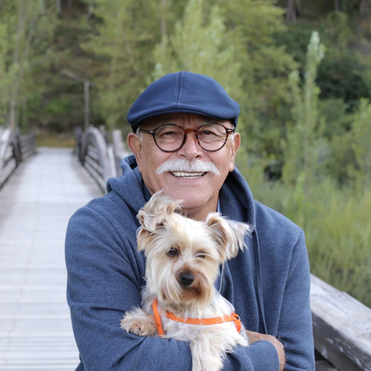 Smiling older man holding a dog on a cold, windy day